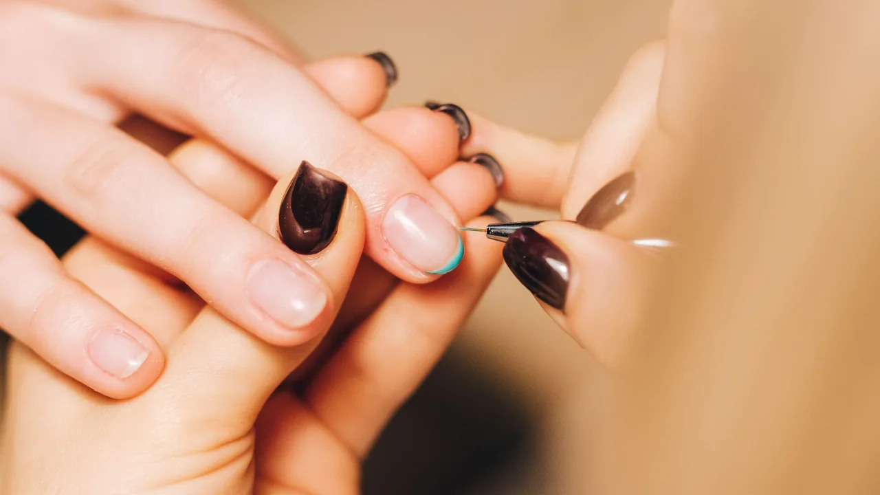 Nail artist carefully painting a client's nails in deep burgundy